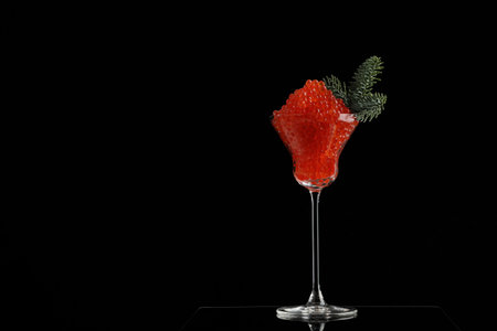 Red caviar in a tall glass. Decoration of a coniferous branch. Salmon caviar. Space for text. Black background. New Years holiday or Christmas.A symbol of wealth and prosperity.の写真素材