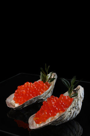 Red caviar is found in oyster shells. Serving snacks with red caviar. A symbol of wealth. A useful omega. Black background. Space for copying.Vertical photo.の写真素材