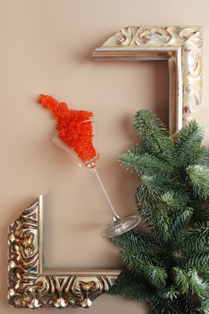 A tall wine glass is filled with red caviar. Caviar fell out of the wine glass. A composition with fir branches and a frame for a picture. A symbol of wealth. A useful omega. New Year or Christmas.の写真素材
