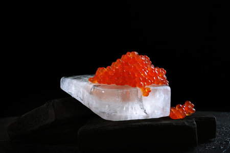 Red caviar on a large piece of ice. Photo on a black background. Salmon caviar. Delicacies. A festive snack. A useful omega. Space for text.の写真素材