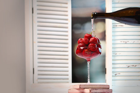 Strawberries and champagne. Berry in tall glass. Champagne pours on strawberries. Photo on the background of the window.の写真素材
