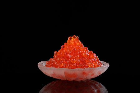 Red caviar in a transparent dish in the form of a shell on a black background. An exquisite snack. Side view.Copy space.の写真素材