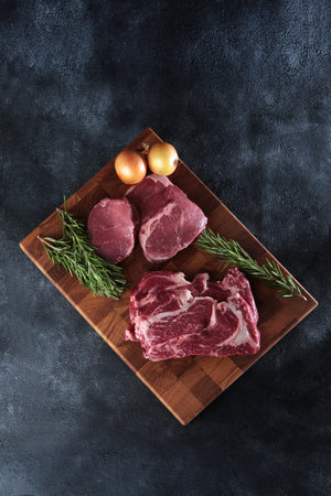 Fresh raw meat. Beef tenderloin.Two types of beef tenderloin on a wooden board. Juicy pieces of meat. A sprig of rosemary and onion. Vertical photo.の写真素材