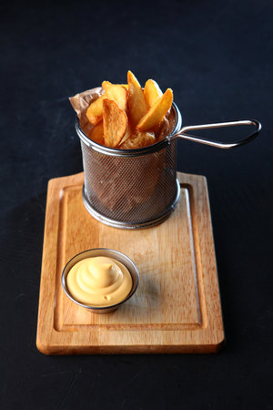 French fries. Potato slices in a basket on a wooden board. Dark background.Photos for the menu. Appetizer for beer.の写真素材