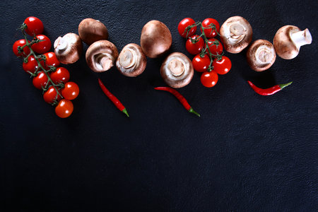 Royal champignons on a dark background. Cherry tomatoes and champignons on a dark background. Red chili pepper.Flat lay.Top view. Copy space.の写真素材