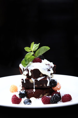 Brownie chocolate sponge cakes with walnuts and melted chocolate, laid out in a stack. The dessert is decorated with a sprig of mint.Vertical photo.の写真素材