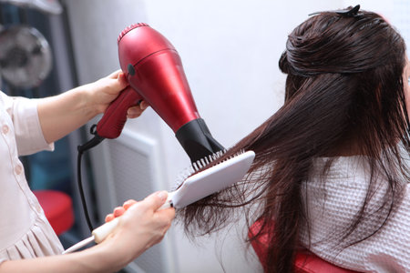 Long hair is styled with a hair dryer. A woman in a beauty salon. Long dark hair.Brush close-up.The concept of beauty salons.の写真素材