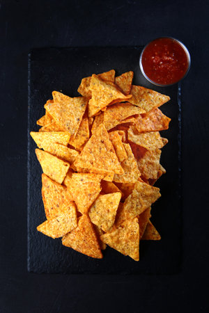 Triangular shaped chips with sauce. Corn chips. Fast food. Appetizer for beer. Vertical photo on black background.の写真素材
