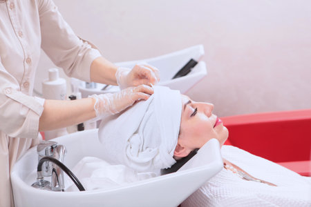 The hair is wrapped in a white towel after the treatment procedure . Woman washes her hair in a beauty salon. Hair care. The concept of spa treatments for hair.の写真素材