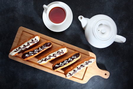 Eclairs on a wooden board. Delicious pastries. Tea in a white teapot.Flat lay.Top view.