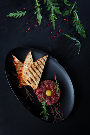 Beef tartar with quail egg and arugula. Black background.Copy space.Flat lay.French cuisine.の写真素材