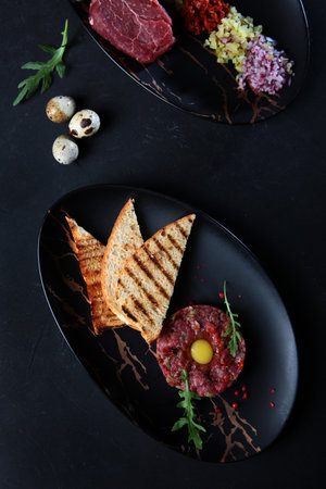Marble beef tartare. Marbled beef tenderloin with capers, red onion, mustard dressing and quail yolk. Served with bread toasts. Flat lay.Top view.Vertical photo.の写真素材