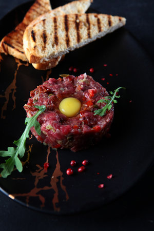 Beef tartare with raw egg yolk, pickled cucumber and onion.Served with bread toasts. French cuisine.Close-up.の写真素材