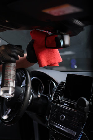 Cleaning the car interior. The rearview mirror is wiped with a microfiber cloth. The concept of cleanliness and disinfection. Vertical photo.の写真素材