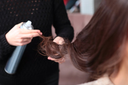 A professional hairdresser applies hairspray to a young womans hair. Hair styling in a beauty salon. Fixation of curls. The concept of beauty.の写真素材