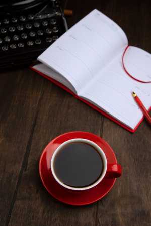 Red cup with coffee. Top view. An old vintage typewriter and an empty piece of paper. Notepad and red pen are out of focus. Concept of business breakfast.の写真素材