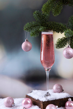 Glass of champagne. Sparkling rose wine in glass. Celebrating with glass of pink champagne. Pink Christmas balls on Christmas tree. New Year card.の写真素材