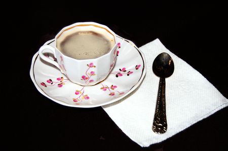 A cup of coffee, a napkin and spoon on a black backgroundの写真素材