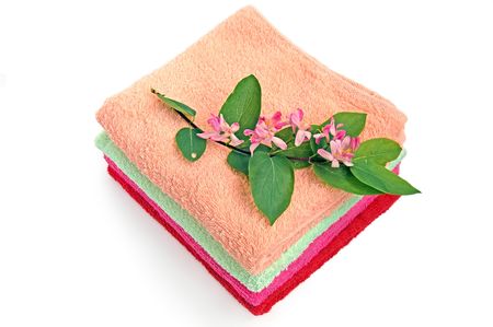 A pile of colorful towels, a sprig of pink flowers and green leaves on a white backgroundの写真素材