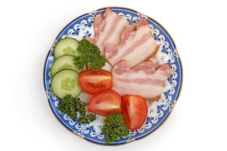 Slices of bacon with slices of cucumbers, tomatoes and sprigs of green parsley on porcelain plate on a white backgroundの写真素材
