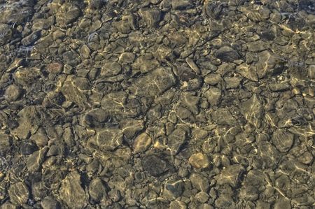 The texture of the large and small stones on the river bottom and the reflection on the water surfaceの写真素材