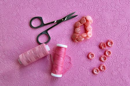 Pink spool of thread, needles, scissors, pink buttons on the background of a pink patterned fabricの写真素材