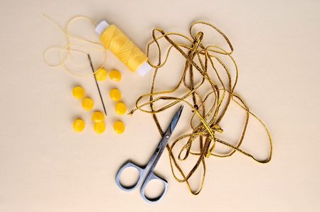 Yellow spool of thread, needles, scissors, yellow buttons, a golden braid on the background of beige silk fabricの写真素材