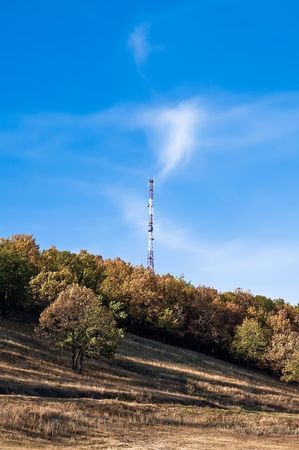 Holm, yellow and brown trees, tower communications on a background of blue sky and white cloudsの写真素材