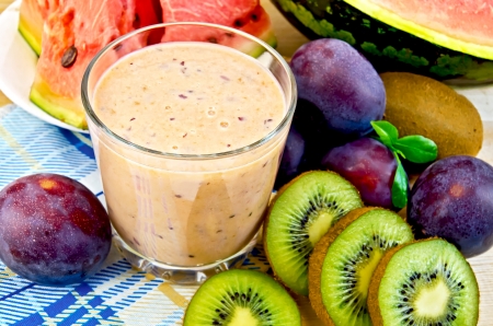 Milk shake in a glass beaker with plums, kiwi and watermelon on a napkin on the background of wooden boards Milk shake in a glass beaker with plums, kiwi and watermelon on a napkin on the background of wooden boards