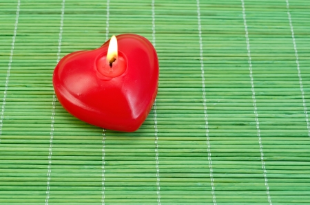 Red candle in the shape of a heart on a green bamboo matの写真素材