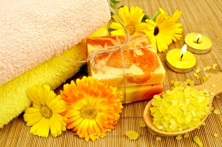 Two bars of homemade soap, towels, bath salt in wooden spoon, two candles and calendula flowers on a background of bamboo napkinsの写真素材