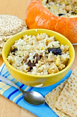 Rice porridge with dried fruit, two small loaves of bread and a spoon on a napkin, stuffed pumpkin, round cereal bread on a wooden boardの写真素材