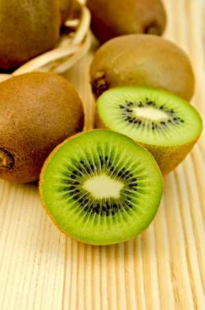 Whole and half kiwi fruit in a wicker plate on a wooden boardの写真素材