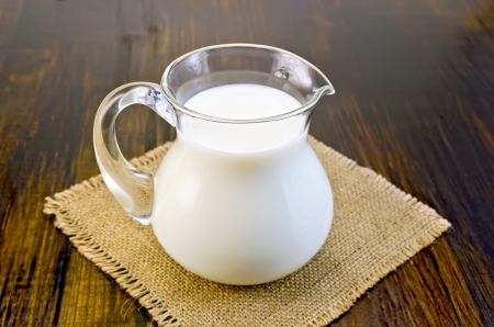 Milk in a glass jug on a napkin from burlap on background dark wooden boardの写真素材