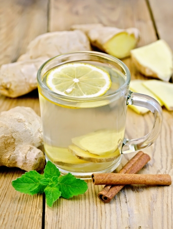 Ginger tea with lemon in a glass mug, mint, cinnamon, ginger root on a wooden boardの写真素材