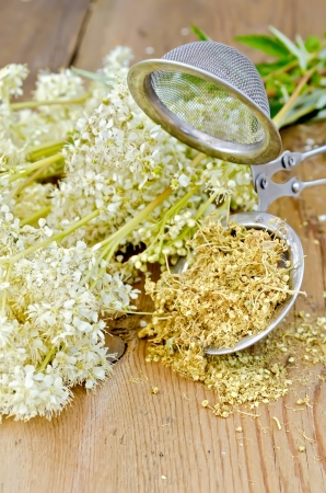 Metal strainer with dried flowers of meadowsweet, a bouquet of fresh flowers of meadowsweet against a wooden boardの写真素材