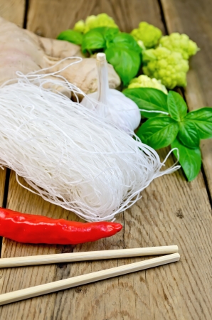 Thin rice noodles with garlic, hot red pepper, ginger, basil and broccoli, chopsticks on a background of wooden boardsの写真素材
