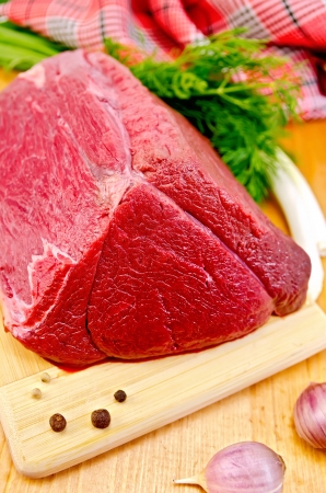 A piece of beef, garlic, peas pepper, dill, chives, napkin, knife on a wooden boardの写真素材