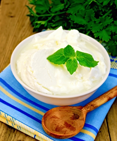 Thick yogurt in a white bowl, parsley, spoon, napkin, mint on the background of wooden boardsの写真素材