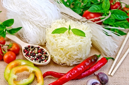 Rice noodles are different, tomatoes, peppers, chopsticks, garlic, basil on a background of sack...
