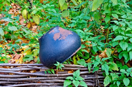 Old cast iron pot on the fence on the background of green grass and yellow autumn leavesの写真素材