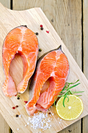 Two pieces of trout with rosemary, coarse salt and lemon on the background of wooden boardsの写真素材