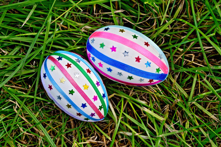 Two easter eggs, decorated with multicolored braid and sparkles as asterisks on green grass top