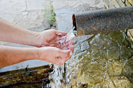 Spring water flows from the pipe into the hands of the men on the background of stoneの写真素材
