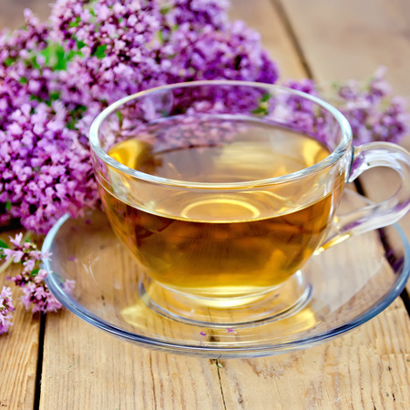 Herbal tea in a glass cup, fresh oregano flowers on a wooden boardの写真素材