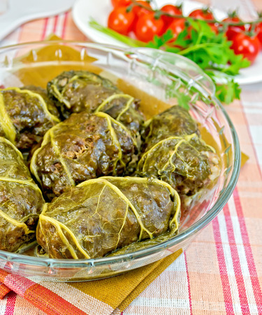 Stuffed cabbage with meat and rhubarb leaves in a glass dish, parsley, tomatoes on a cloth backgroundの写真素材