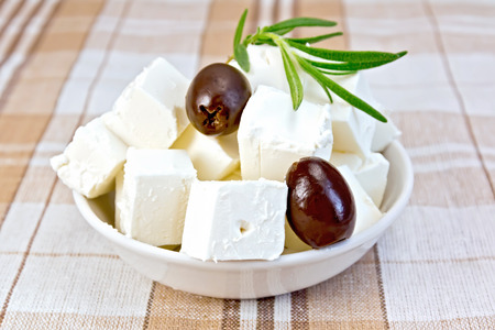 Feta cheese, olives, rosemary in a white bowl on a background of brown tableclothの写真素材