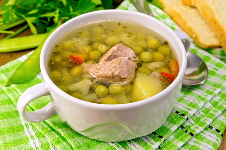 Green pea soup with meat and potatoes in a white bowl, bread, spoon, parsley on a green napkin on the background of wooden boardsの写真素材