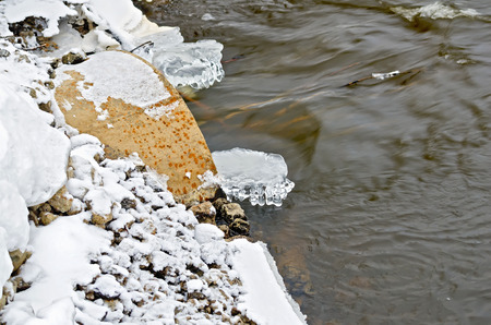 Rocky snowy shore with rusty iron pipes with poured water flowの写真素材