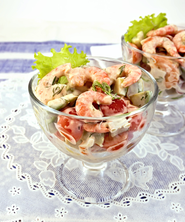 Salad with shrimp, avocado, tomato and mayonnaise, green lettuce in a glass goblet with a silicone napkin, a plate against the background of blue linen tableclothの写真素材